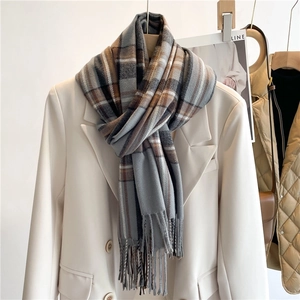 Dettaglio di una sciarpa a quadri grigi con nappe abbinata a un blazer color crema chic