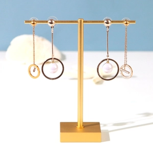 Golden drop earrings with white pearls displayed on a minimalist jewelry stand