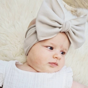 Close-up of baby girl wearing a beige knitted headband with a large bow detail
