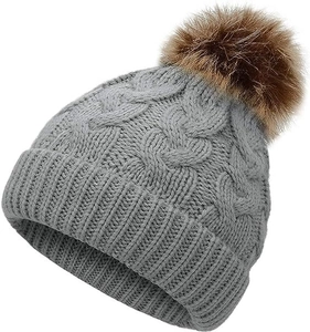 Close-up of grey knit beanie featuring cable knit texture and large brown pom-pom detail