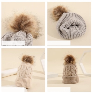 Detail of cable knit baby beanies featuring fluffy faux fur pom poms and thick texture