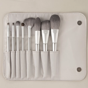 Detail view of 8 professional makeup brushes with silver handles and beige fabric pouch