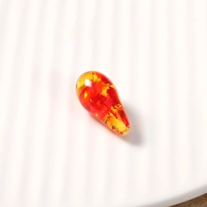 Detailed close-up of a teardrop-shaped amber resin bead with colorful gradient finish
