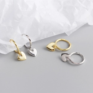 Detail of silver and gold heart pendant hoop earrings on a textured paper surface