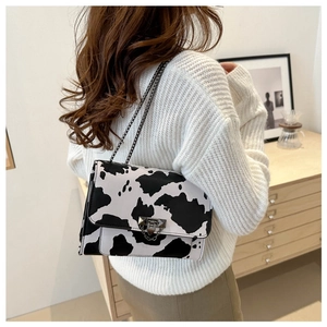 Crossbody bag with cow print pattern and metal chain strap shown in a home setting