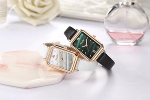 Detail of square gold watches with green and white dials on marble decorative tray