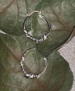 Detail showing silver knot stud earrings on green leaves with stone background