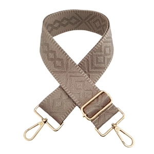 Detail of adjustable khaki woven bag strap with geometric patterns and gold metal buckles