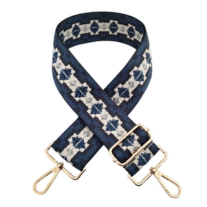 Detail of blue and white geometric jacquard bag strap with gold metal hooks and buckle