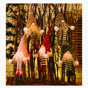 Close-up of four lighted Christmas gnomes with knitted hats hanging on winter branches