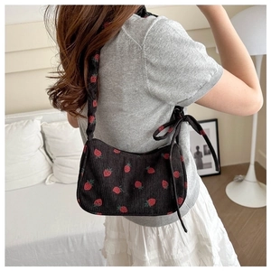 Black corduroy shoulder bag with strawberry embroidery and bow detail on female model
