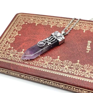 Detail of amethyst hexagonal prism pendant with vintage silver hollow pattern on a notebook