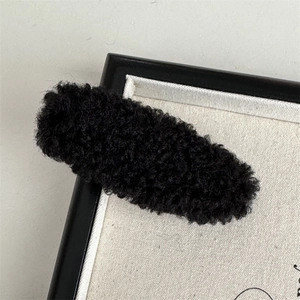 Close-up of a minimalist black plush hair clip with warm autumn winter velvet texture