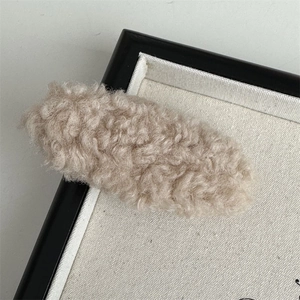 Macro shot of a soft beige plush hair clip on a neutral fabric tray detail view
