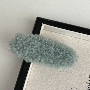 Close-up of a soft plush grey-green oval hair clip with fuzzy texture on a canvas background