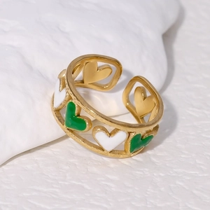 Detail of gold open ring with green and white enamel hearts on textured white background