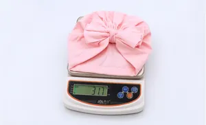 Pink infant turban hat with large bow detail weighing approximately 31.7 grams on a scale