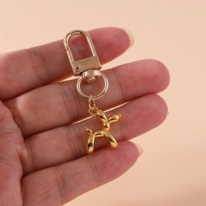 Glossy golden balloon dog keychain with metal lobster clasp held in hand close-up
