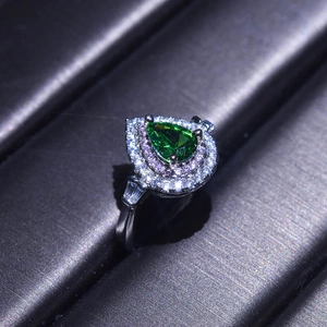 Macro shot of a pear-shaped green emerald ring with silver plating and sparkling diamond halo