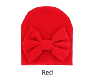 Macro detail of red knitted baby hat featuring a large soft bow on a white background