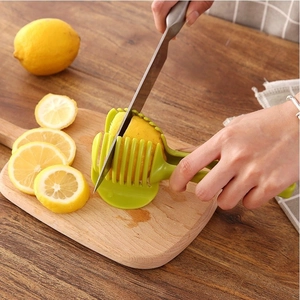 Green plastic lemon slicer holder tool cutting fresh lemon slices on a wooden board