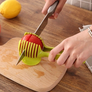 Green handheld tomato and lemon slicer tool used on a wooden board for precise cutting
