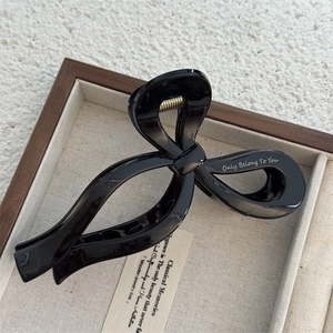 Close-up of a glossy black bow hair claw clip featuring Only Belong To You lettering