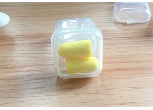 Close-up of a pair of yellow foam earplugs inside a small clear plastic storage box