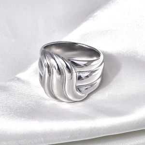 Macro detail of wavy silver titanium steel ring on elegant white silk fabric