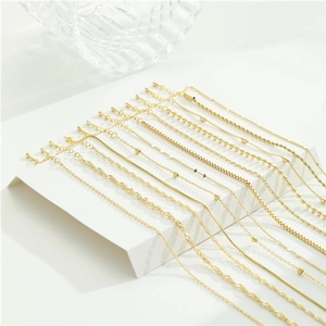 Collection of gold stainless steel necklace chains in various styles on a minimalist display
