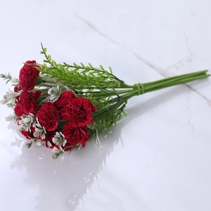 Detail of red artificial carnation bouquet with green leaves on white marble surface