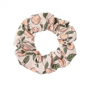 Close-up of soft beige fabric scrunchie featuring cute hand-painted peach and flower patterns