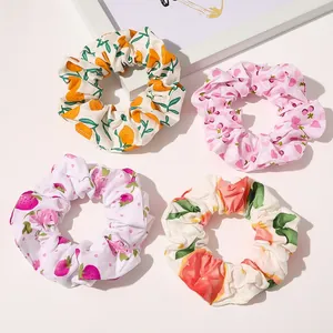 Detail shot of four cotton fabric scrunchies with orange, floral, and fruit patterns