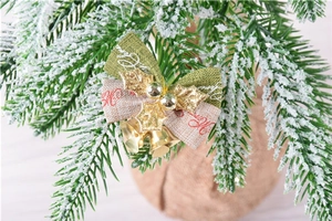 Close-up of green and gold Merry Christmas bow with metal bells on snowy pine tree branches