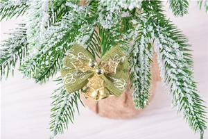 Detail of green Christmas bow with golden bells and holly leaves on snow-covered pine