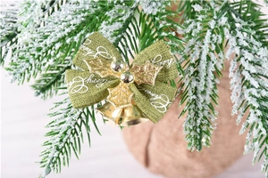 Macro view of green fabric Christmas bow with gold holly leaves and small metal bells