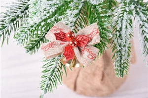 Close-up of linen Christmas bow with red Merry text, glitter leaves and gold bells