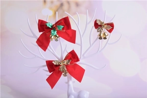 Three red velvet Christmas bows with holly leaves and gold bells on a white display stand