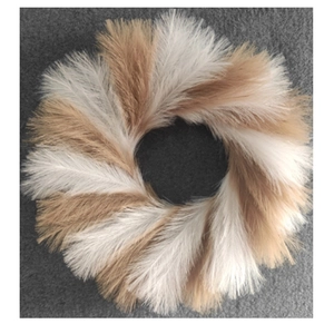 Top view of faux reed Christmas wreath with white and light brown feathers on grey fabric