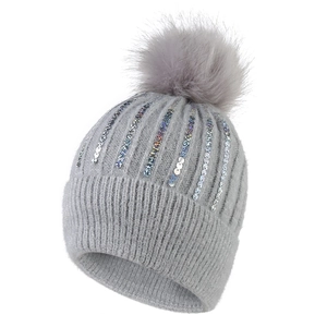 Détail d'un bonnet en tricot gris avec paillettes colorées et pompon en fausse fourrure