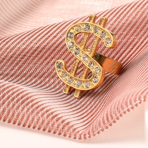 Macro view of gold dollar sign ring with crystals on rose gold textured fabric