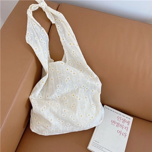 Close-up of white daisy floral canvas tote bag with stylish knot strap on brown sofa