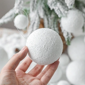 White foam Christmas snowballs with velvet flocking hanging from a pine branch
