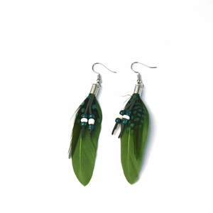 Detail of green feather earrings with ethnic beads and silver hooks in bohemian style