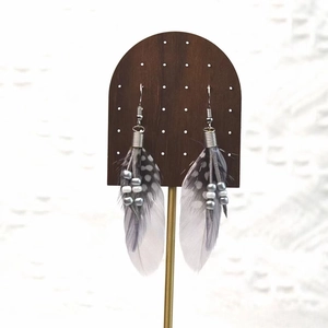 Detail of bohemian long feather earrings with grey spots and silver hooks on wood display