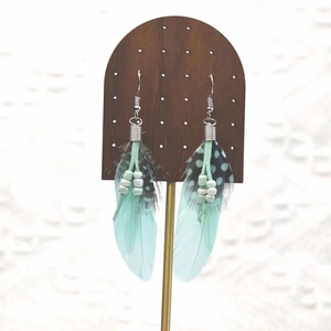 Detail of bohemian long feather earrings with turquoise beads on a wooden stand
