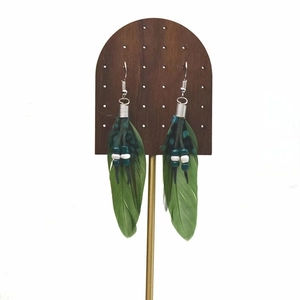 Detail of bohemian long green feather earrings with beads on a wooden display stand