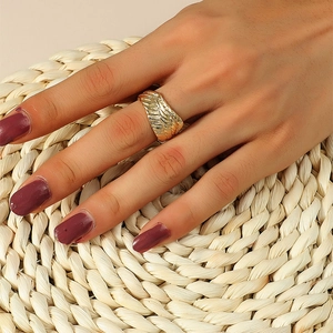 Close-up of golden angel wing ring with feather texture worn on hand over straw mat