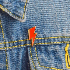 Detail of red lightning enamel pin with gold plating on blue denim jacket pocket