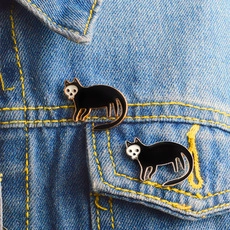 Close-up of punk black enamel cat skull pins on blue denim fabric background